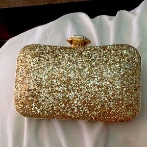 A gold clutch purse with a gold strap.